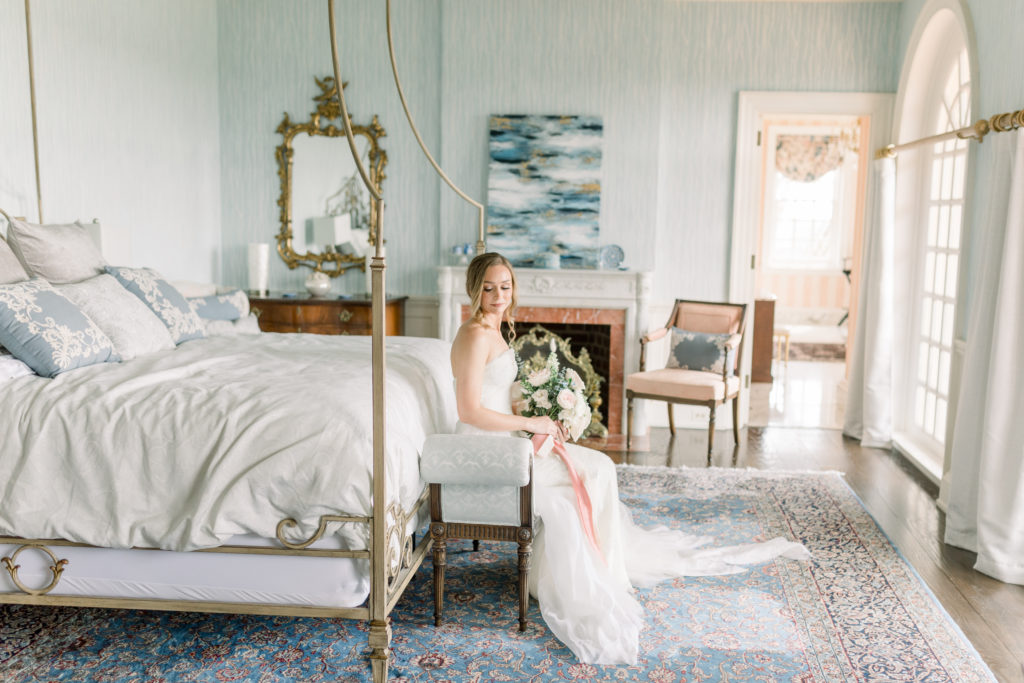The Estate at River Run Wedding, Bride sitting on a bed holding wedding florals